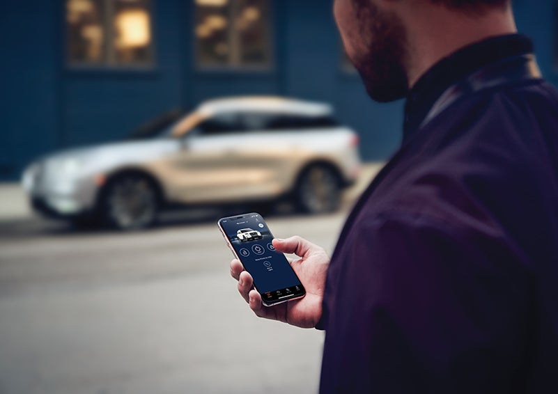 A person is shown interacting with a smartphone to connect to a Lincoln vehicle across the street. | Vista Lincoln Woodland Hills in Woodland Hills CA